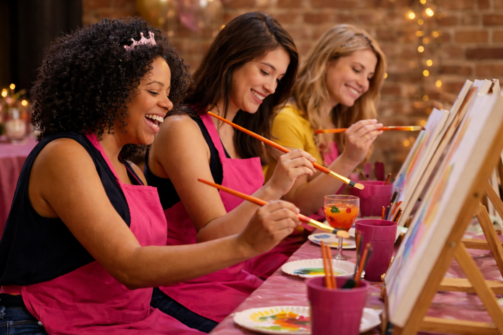 three women celebrating a bachelorette party while painting and smiling.
